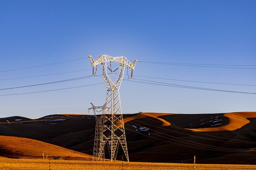 阿里地區(qū)的曠野上，電力鐵塔在夕陽下熠熠生輝。